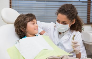 Pediatric dentist showing little boy in chair the drill at the dental clinic