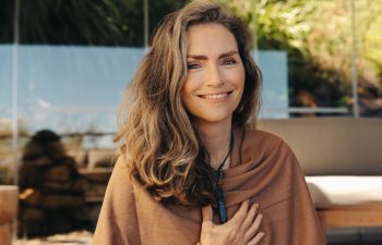 Cheerful senior woman smiling at the camera while wearing a crystal necklace. Happy woman meditating and practicing crystal healing on her chest chakra. Mature woman following a holistic lifestyle.