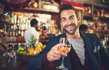 Portrait, wine and man in bar, happiness and stress relief with joy, date and cheers for achievement. Face, person and customer with alcohol, glasses and toast in restaurant, relaxing and excited.